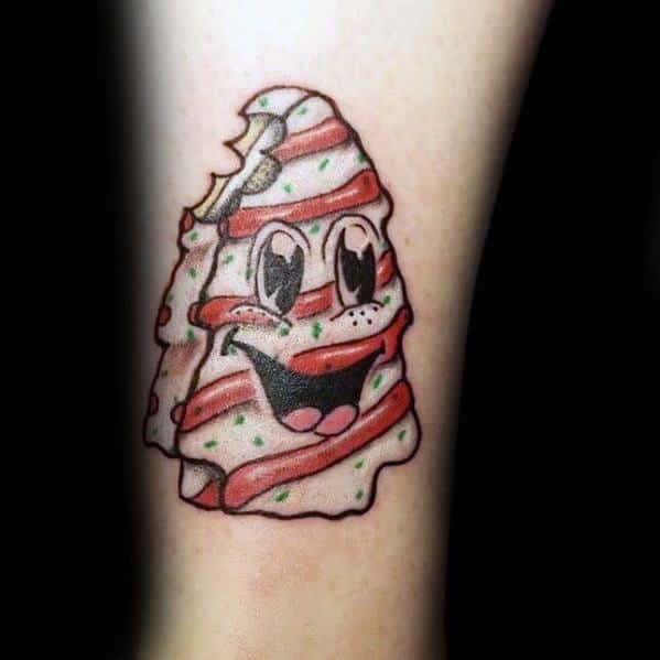 Playful Christmas tree cookie tattoo with candy cane stripes, a smiling face, and a bite mark, creating a fun and festive holiday design.