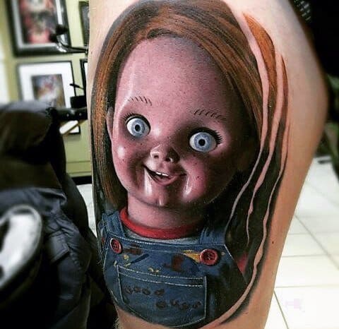 Realistic Chucky tattoo with vivid details, featuring his unsettling wide-eyed stare, eerie grin, and blood-stained overalls for a chilling horror design.
