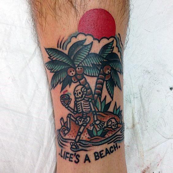 Playful beach tattoo of skeletons lounging under coconut trees with a red sun and the phrase “Life’s a Beach” inked below.