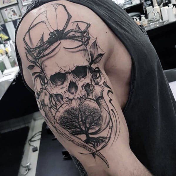 Black and grey upper arm tattoo featuring a detailed skull with antlers, a tree inside a crystal ball, and flowing abstract elements, symbolizing life and death.