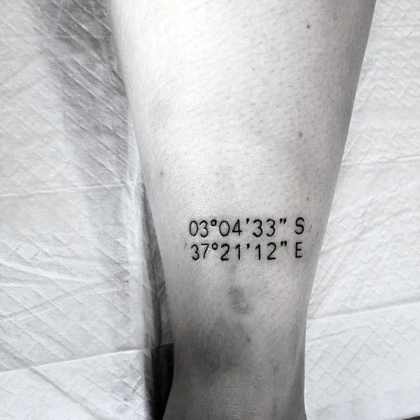 Minimalist coordinate tattoo on the leg with clean black lettering, marking a significant location with a simple and elegant design.