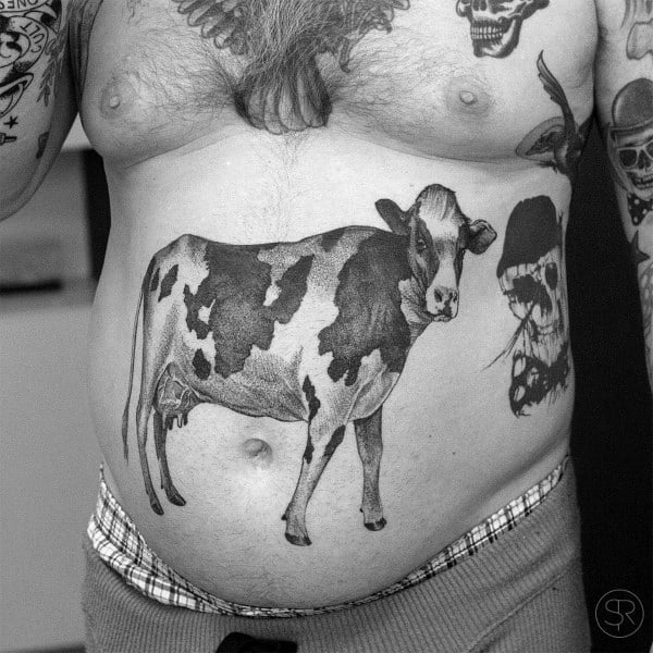 Realistic black and grey cow tattoo placed prominently on the stomach, featuring detailed shading and natural proportions.
