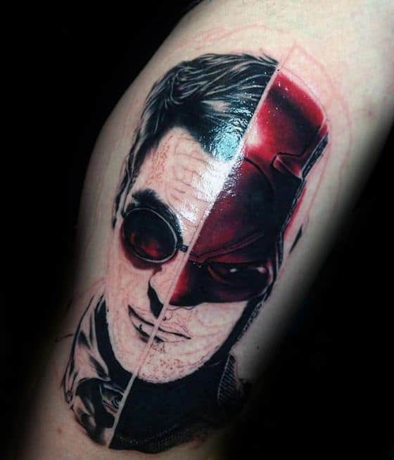Split-face tattoo of Matt Murdock and Daredevil, blending black and grey realism with bold red tones to show his dual identity.