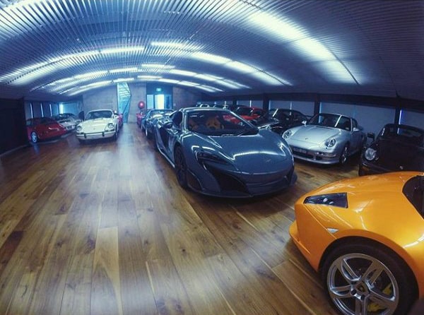 A masculine dream garage featuring polished wood flooring and a collection of exotic cars, illuminated by sleek overhead lighting.