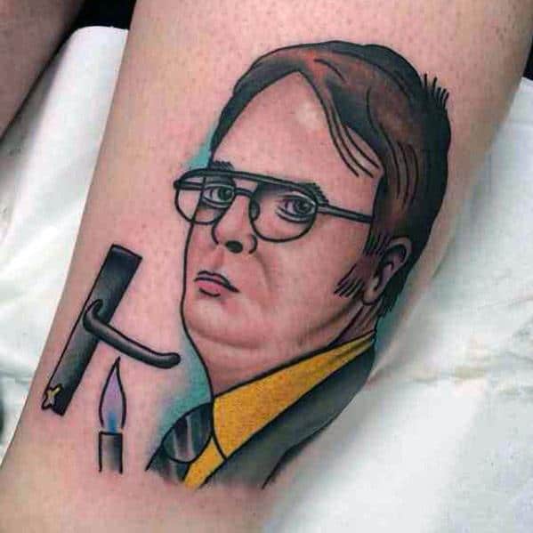 Tattoo of Dwight Schrute with a serious expression, wearing glasses and a yellow shirt, featuring a broken door handle and a candle beside him.