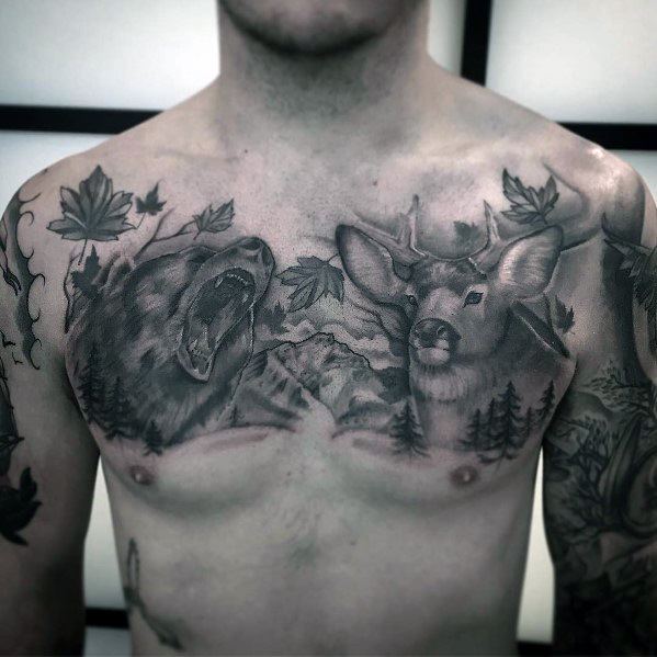 Realistic black and grey chest tattoo featuring a roaring bear, an elk, mountains, trees, and falling leaves for a bold wildlife-inspired design.