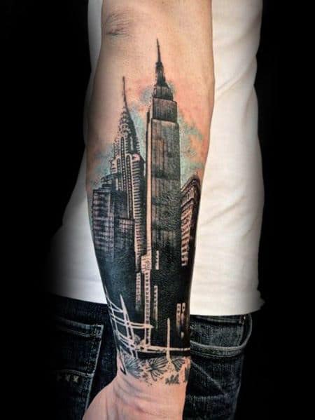 Empire State Building tattoo featuring a detailed city skyline and subtle color accents, extending prominently on a man's outer forearm.