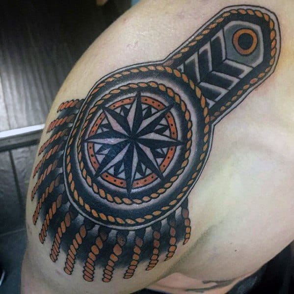 Color epaulette tattoo featuring a bold compass rose, orange and black braided details, and thick tassels over the shoulder.