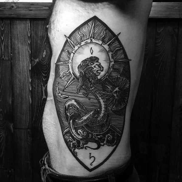 Tattoo of a roaring sea serpent under a radiant sun, framed in an oval shield with waves, celestial details, and astrological symbols.
