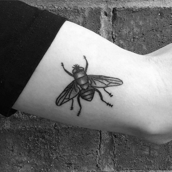 Small realistic fly tattoo on the ankle with fine linework and soft shading, positioned to look like the insect just landed.