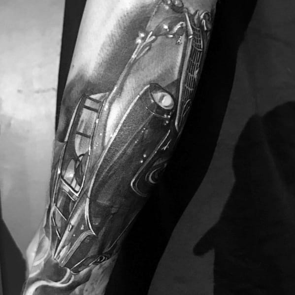 Realistic black and grey Ford Mustang tattoo on forearm, featuring a dynamic angled perspective with intricate shading and fine automotive details.