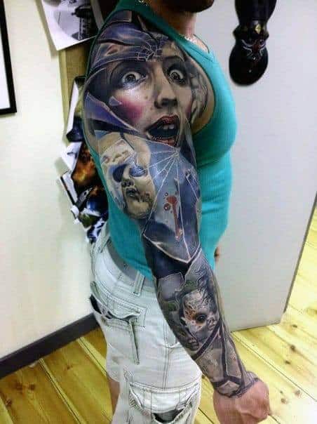 Full sleeve tattoo with a dramatic, shattered glass effect featuring expressive female faces, cracked masks, and surreal elements in vivid color.