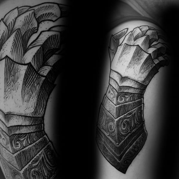 Detailed blackwork tattoo of an ornate medieval gauntlet on the upper arm, featuring intricate patterns and fine line shading.