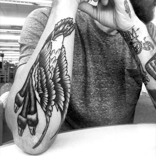 Black and gray tattoo of two geese in flight, inked on the forearm with intricate feather detailing and bold shading for a dynamic look.