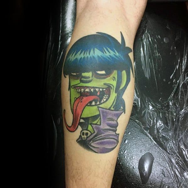 Vibrant color tattoo of Murdoc from Gorillaz with green skin, blue hair, exaggerated tongue out, and a purple collar with a skull detail.