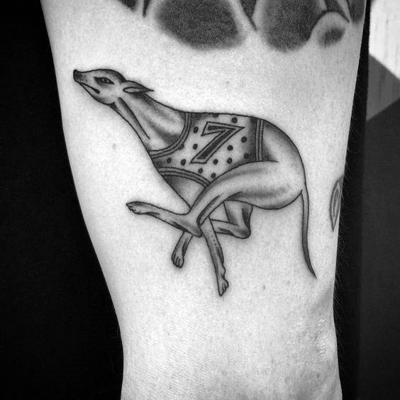 A sleek black and white tattoo of a greyhound in motion, featuring a number "7" on its racing vest, emphasizing its speed and athleticism.