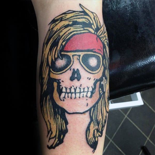 Bold tattoo of a cartoon-style skull with long blonde hair, sunglasses, and a red bandana, inspired by Axl Rose of Guns N' Roses.