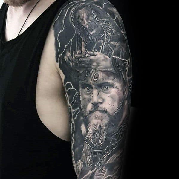 A detailed black and white tattoo on an arm depicting a bearded man and another figure with hands raised