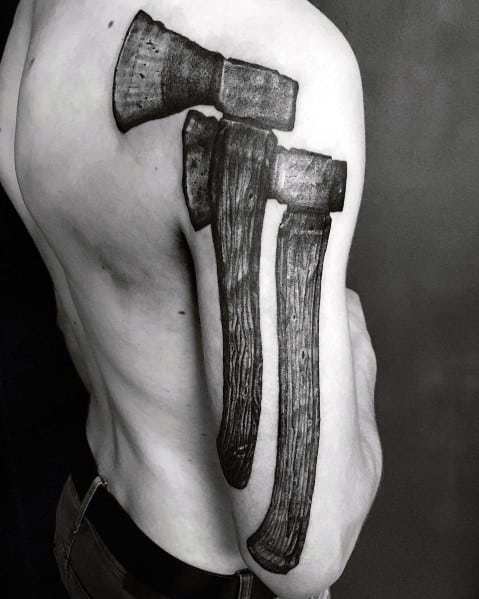 Black and grey tattoo featuring three realistic hatchets inked along the shoulder and upper arm, with detailed wood grain handles and rugged blades.