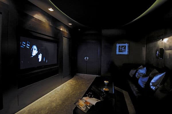 Cozy home theater with dim lighting, a movie on screen, and seating adorned with decorative pillows