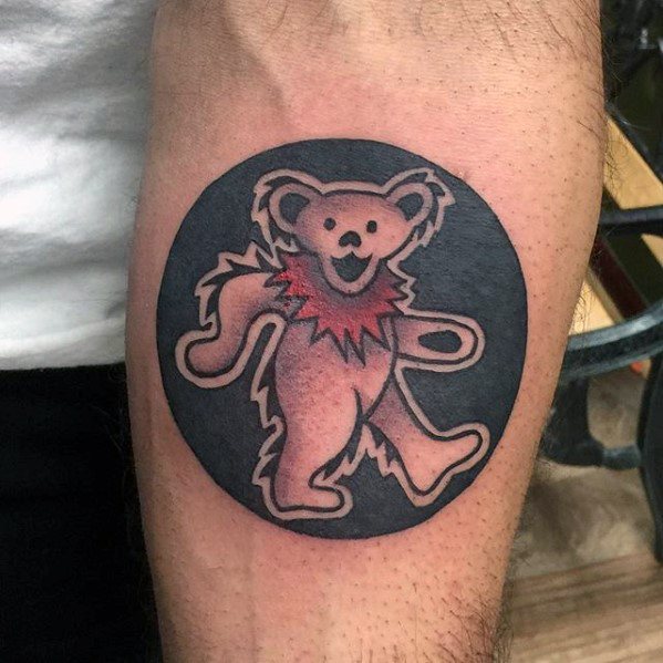 Dancing pink Grateful Dead bear tattoo inside a dark circle, placed on the upper arm with subtle shading and bold outline.