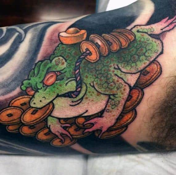 Japanese-style tattoo featuring a green fortune toad sitting on a pile of gold coins, with a rope around its neck, symbolizing prosperity and good luck.