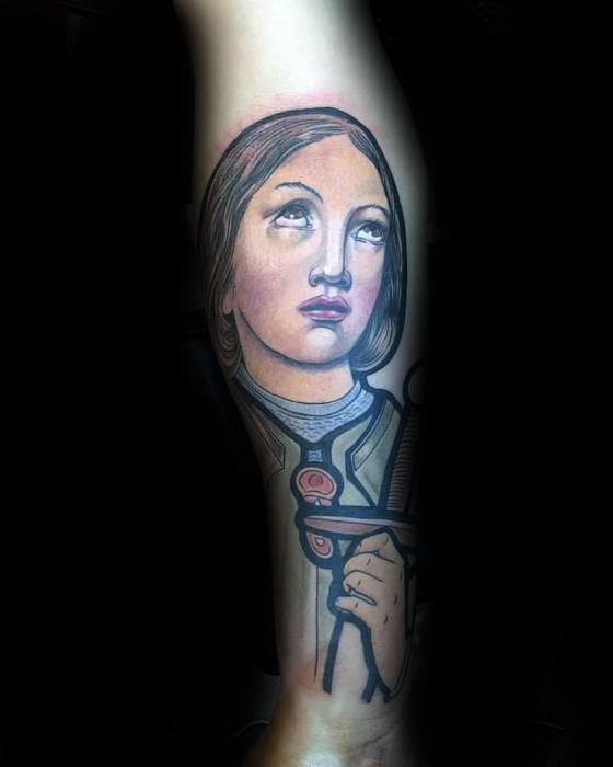 Color tattoo of Joan of Arc in stained glass style, gazing upward with a sword in hand and soft shading emphasizing a serene expression.