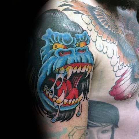 Bold neo-traditional King Kong tattoo on upper arm with a blue face, exaggerated features, dripping saliva, and vibrant red and yellow tones.