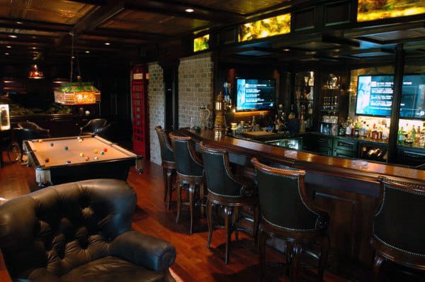 A cozy bar with a pool table, leather chairs, and a well-stocked shelf in a dimly lit room