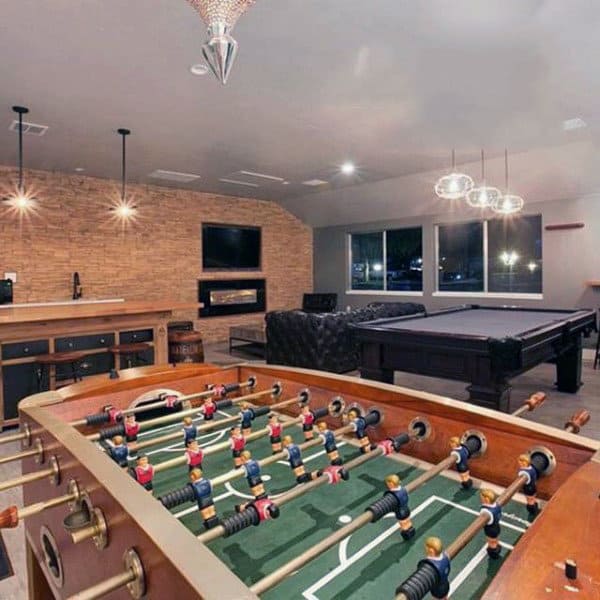 Stylish game room with foosball and pool tables, a bar, brick wall, and modern lighting fixtures