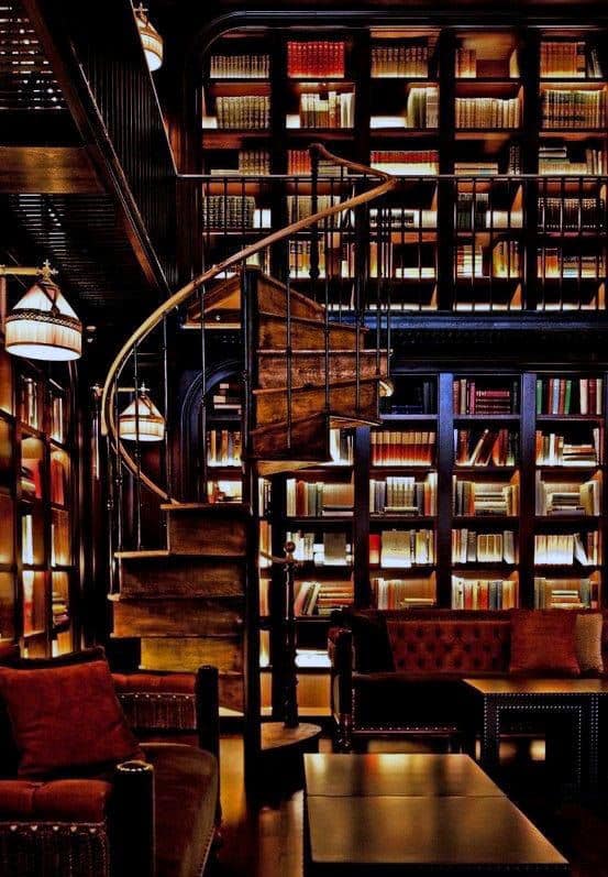 A dimly lit library with a spiral staircase, bookshelves full of books, and cozy armchairs surrounding a table
