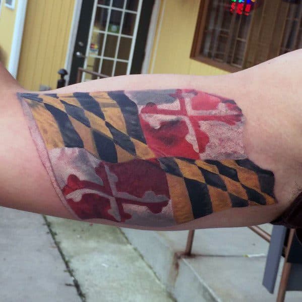 Maryland flag tattoo on the forearm with a worn and faded effect, giving it a vintage and rugged appearance while showcasing state pride.