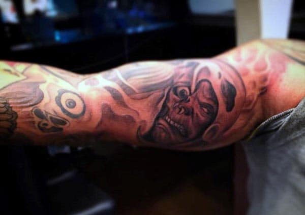 Dark and fiery tattoo of a grim reaper with a skull face emerging from swirling flames, creating a bold and intense design on the bicep