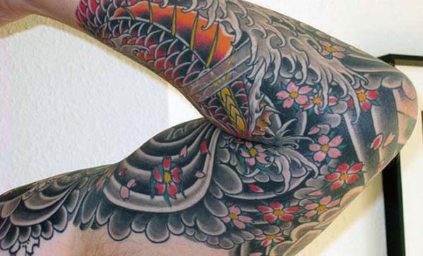 Arm with vibrant full-sleeve tattoo featuring floral and Japanese-inspired designs