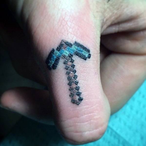 Small Minecraft diamond pickaxe tattoo on the side of the thumb, done in a pixelated style with black and teal blocky shading.