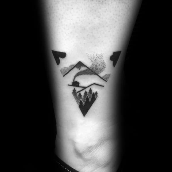 Geometric mountain tattoo on the wrist, featuring bold black shapes, dot shading, trees, and a river for a modern and artistic nature-inspired design.