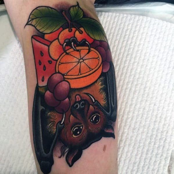 Neo-traditional tattoo of a bat hanging upside down with vibrant fruits like orange slices, watermelon, and grapes above its head.