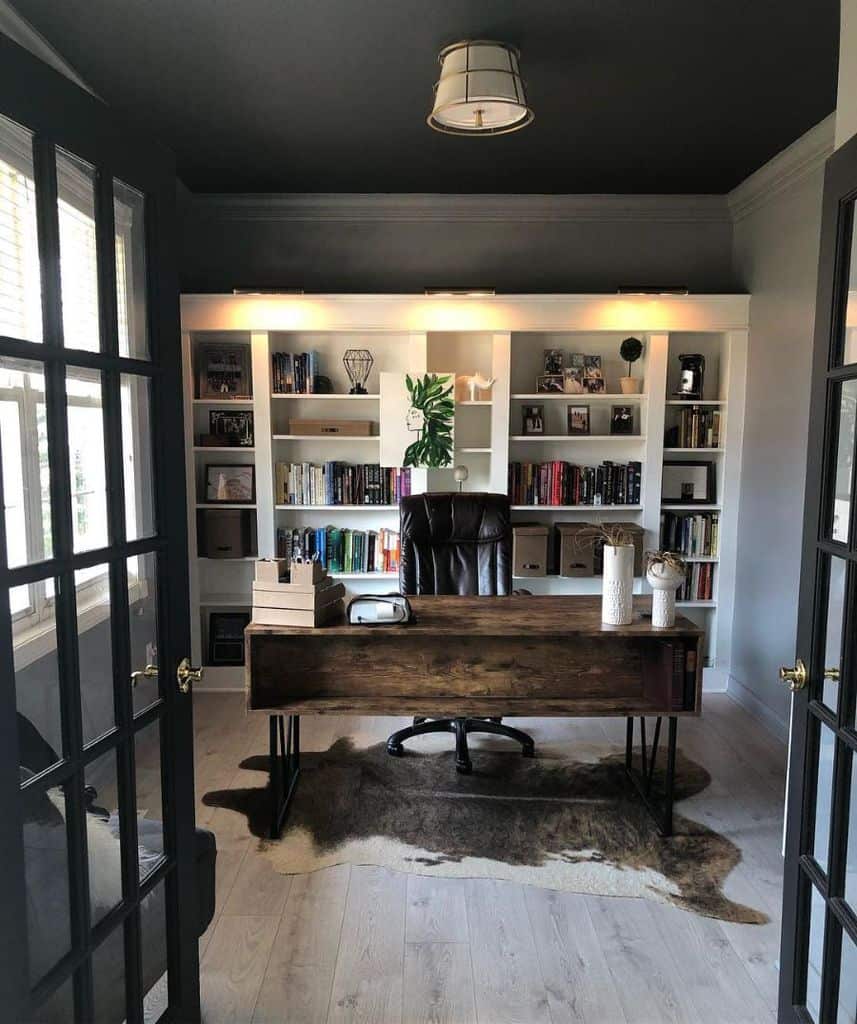 masculine home office wood desk black leather office chair built-in shelving animal hide floor rug