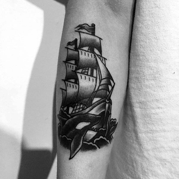 Black and gray tattoo on the forearm featuring an orca whale alongside a detailed ship, with waves and shading to create a dynamic, nautical scene.