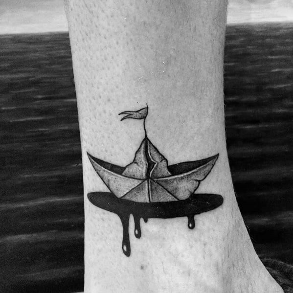 Paper boat tattoo floating on melting black ink, symbolizing fragility, impermanence, and the passage of time.
