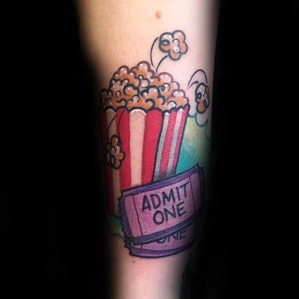 Tattoo of a red-striped popcorn bucket with bouncing kernels and a purple movie ticket reading ADMIT ONE in a playful, colorful style.