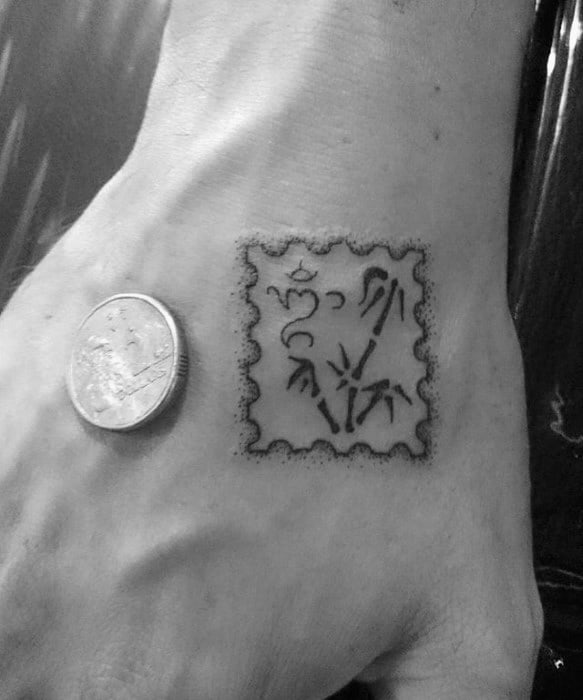 Tattoo of a stylized postage stamp with abstract designs on a hand, next to a coin for size reference