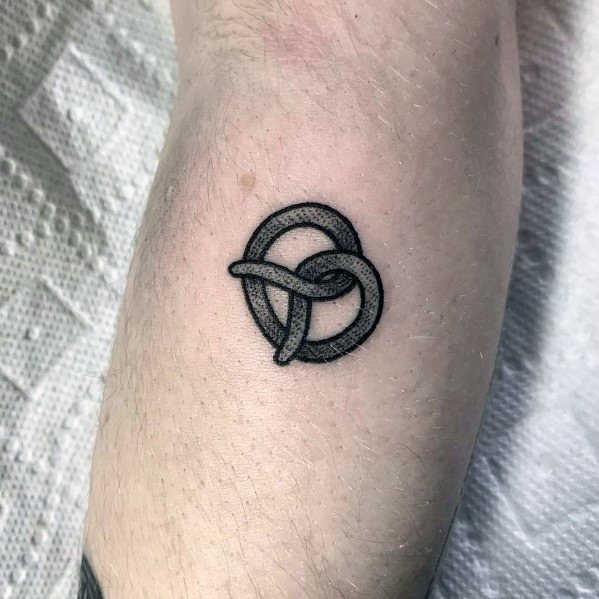 Minimalist black ink pretzel tattoo with fine linework and subtle shading, creating a simple yet bold design on the forearm.