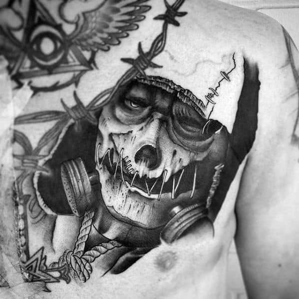 Dark scarecrow chest tattoo with a stitched skull face, gas mask, barbed wire, and intense shading in a gritty black and grey style.