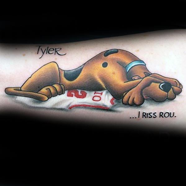 Tattoo of a sad Scooby-Doo lying on a jersey with the name Tyler above and the words "...I riss rou" in tribute style.