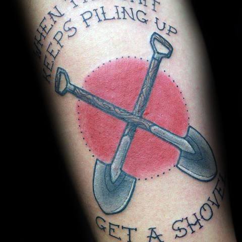 Tattoo of two crossed shovels over a red circle, with the phrase "When the shit keeps piling up, get a shovel," symbolizing resilience.
