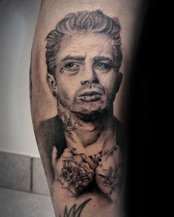 Modernized black and grey tattoo of James Dean with facial tattoos, stretched earlobes, neck ink, and hands in prayer showing knuckle tattoos.