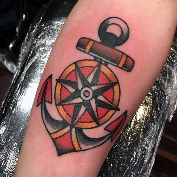 Traditional anchor tattoo with a detailed compass at the center, bold black outlines, red and yellow shading, symbolizing guidance and stability.