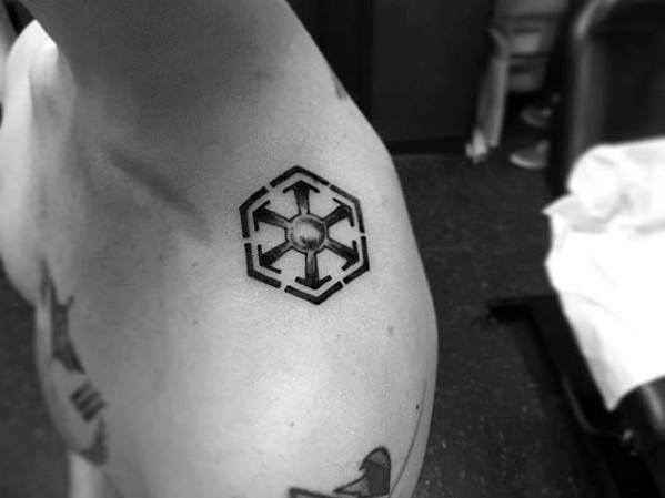 Small Sith Empire symbol tattoo in black ink placed on the upper shoulder, featuring clean lines and subtle shading at the center.