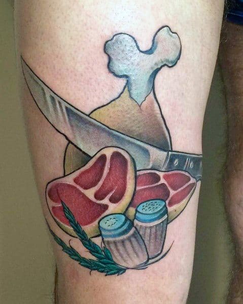 Tattoo of a steak, chicken drumstick, knife, salt and pepper shakers, and herbs, creating a bold and detailed food-themed design